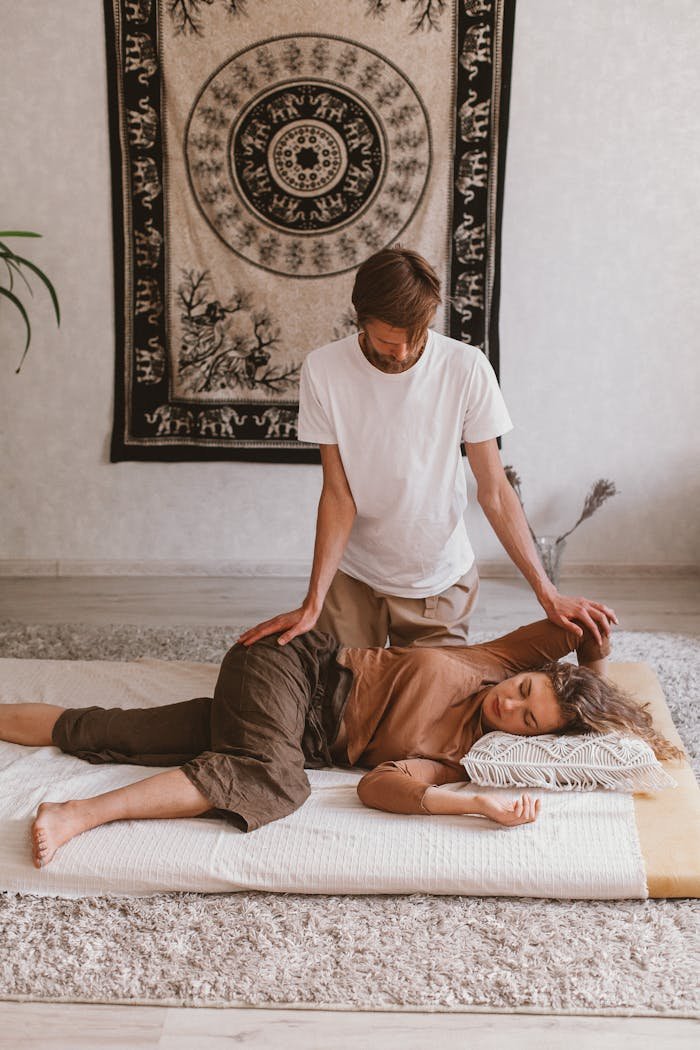 A man giving a massage to a woman lying on the floor, set against a decorative tapestry.